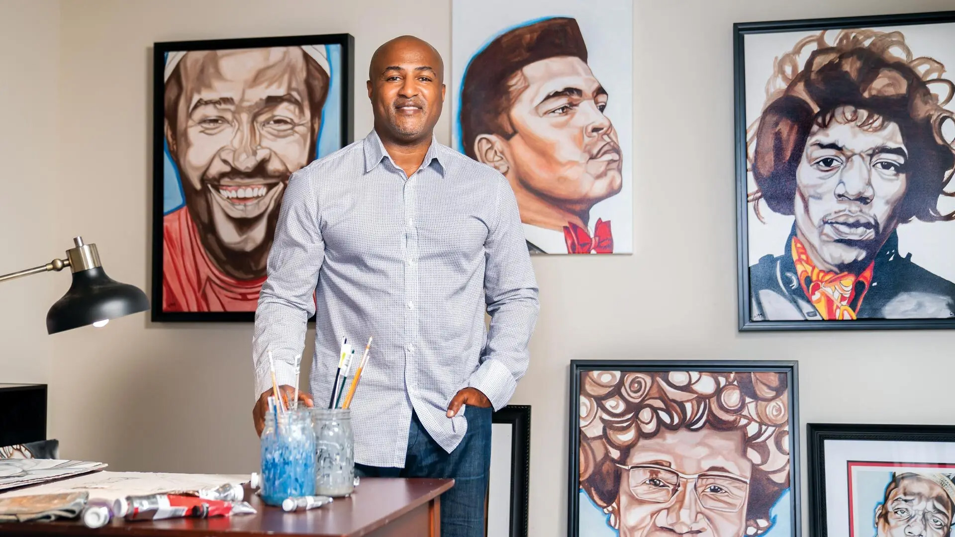 Artist and former Terps football player Lynde Washington '99 poses with a few of the oil paintings he's created over the years, often focusing on African American athletic and cultural luminaries. Photo by Ryan Donnell.